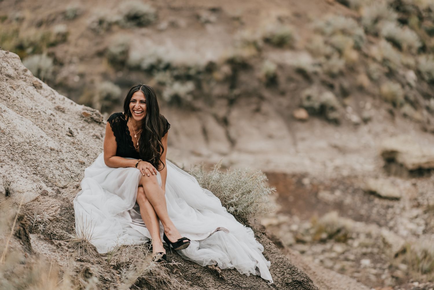 Person in flowing white dress posing on rocky terrain during outdoor photo shoot.