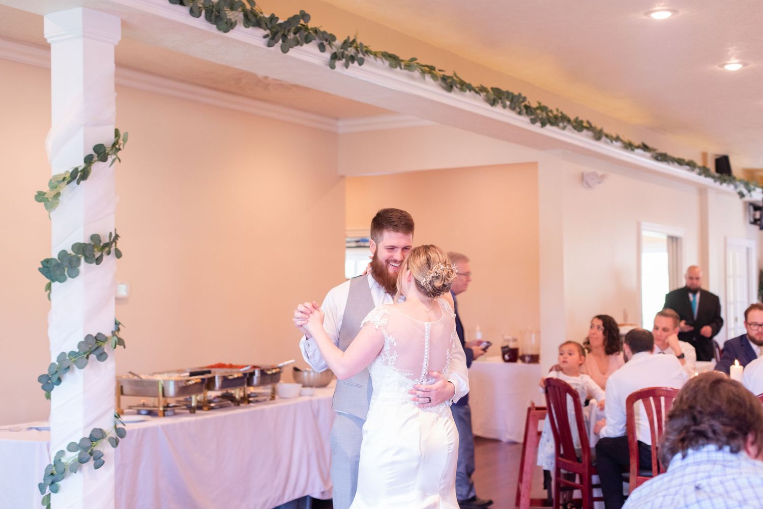 Reception venue decorated with green garland and white tablecloths for a wedding celebration.
