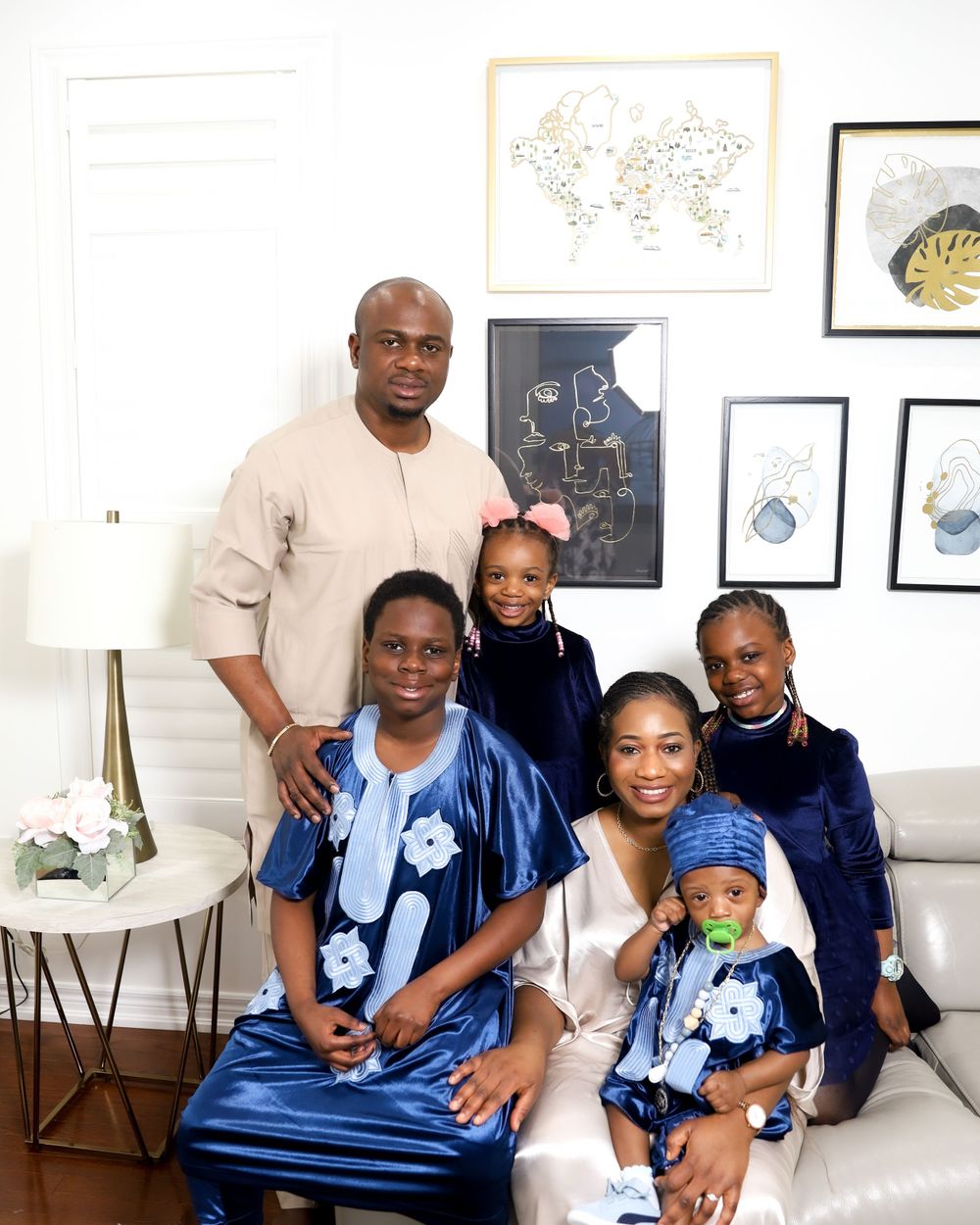 Family wearing coordinating blue and white outfits pose together in living room with framed art.