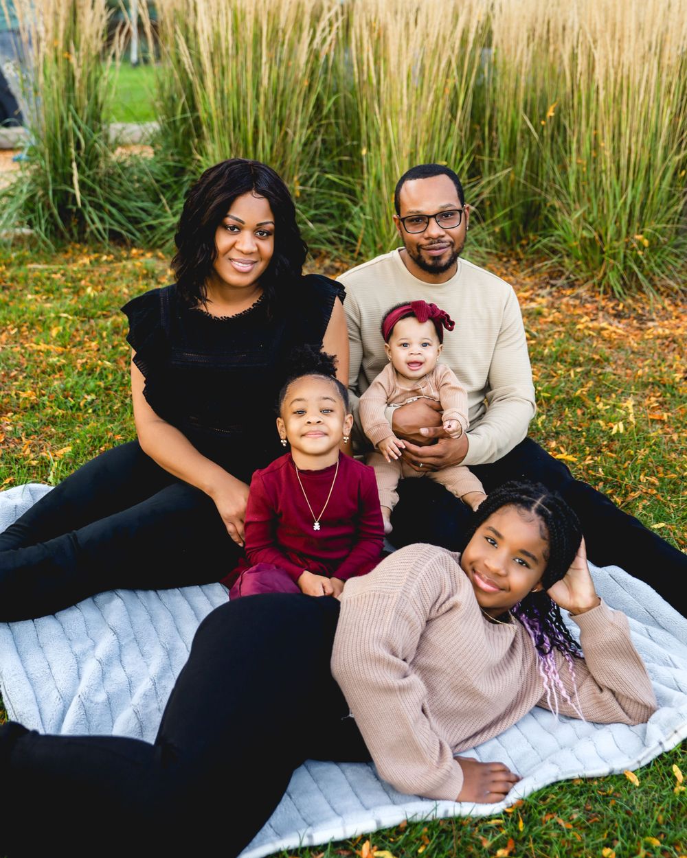 Family relaxing together on a blanket outdoors with tall ornamental grasses in the background.