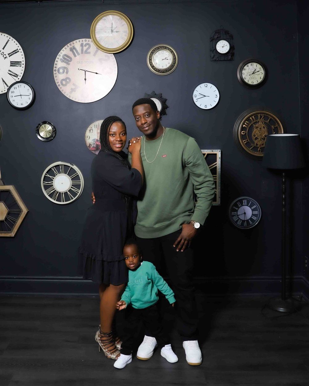 Family portrait against wall decorated with vintage clocks in modern studio setting.