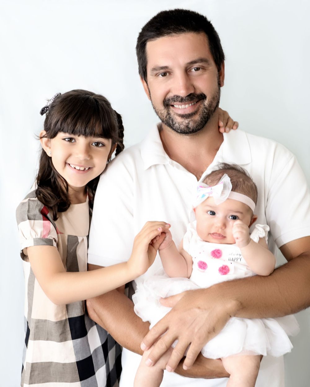 Studio portrait featuring two children with an infant in a white dress.