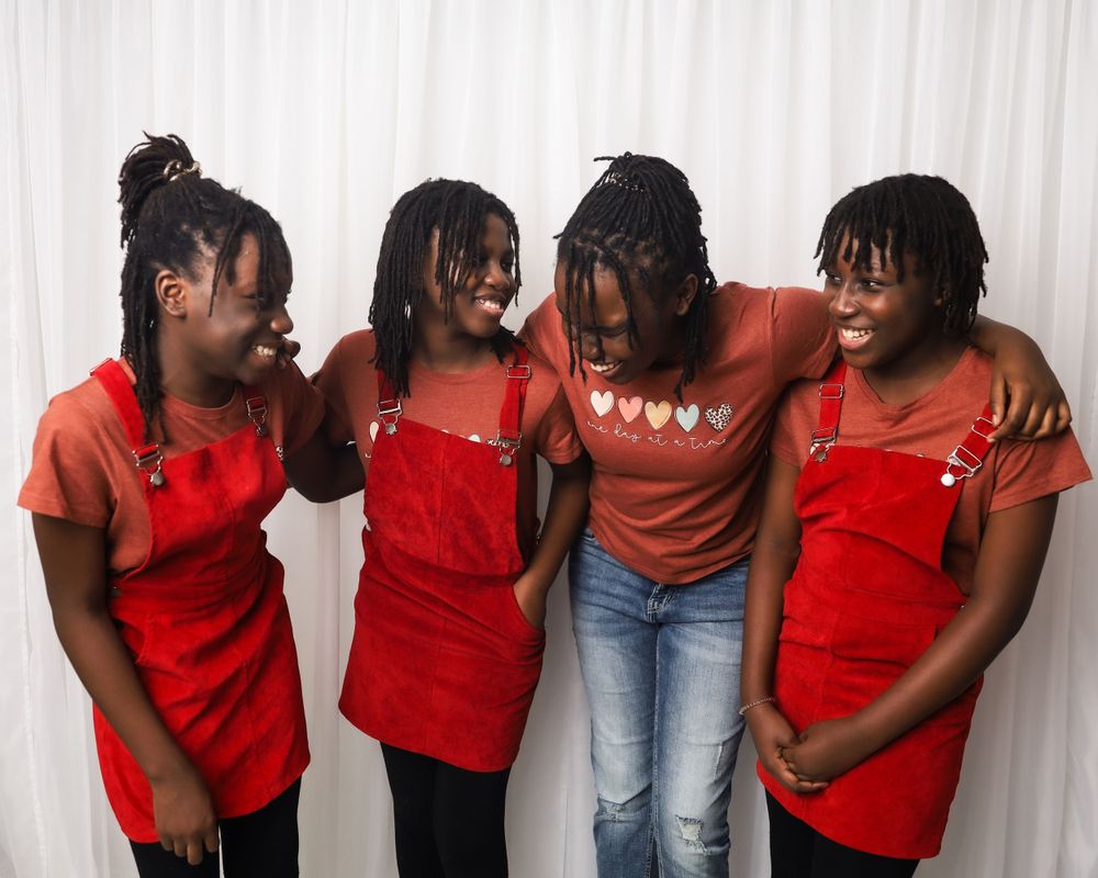 Four people in red tops lean together laughing against a white studio background.