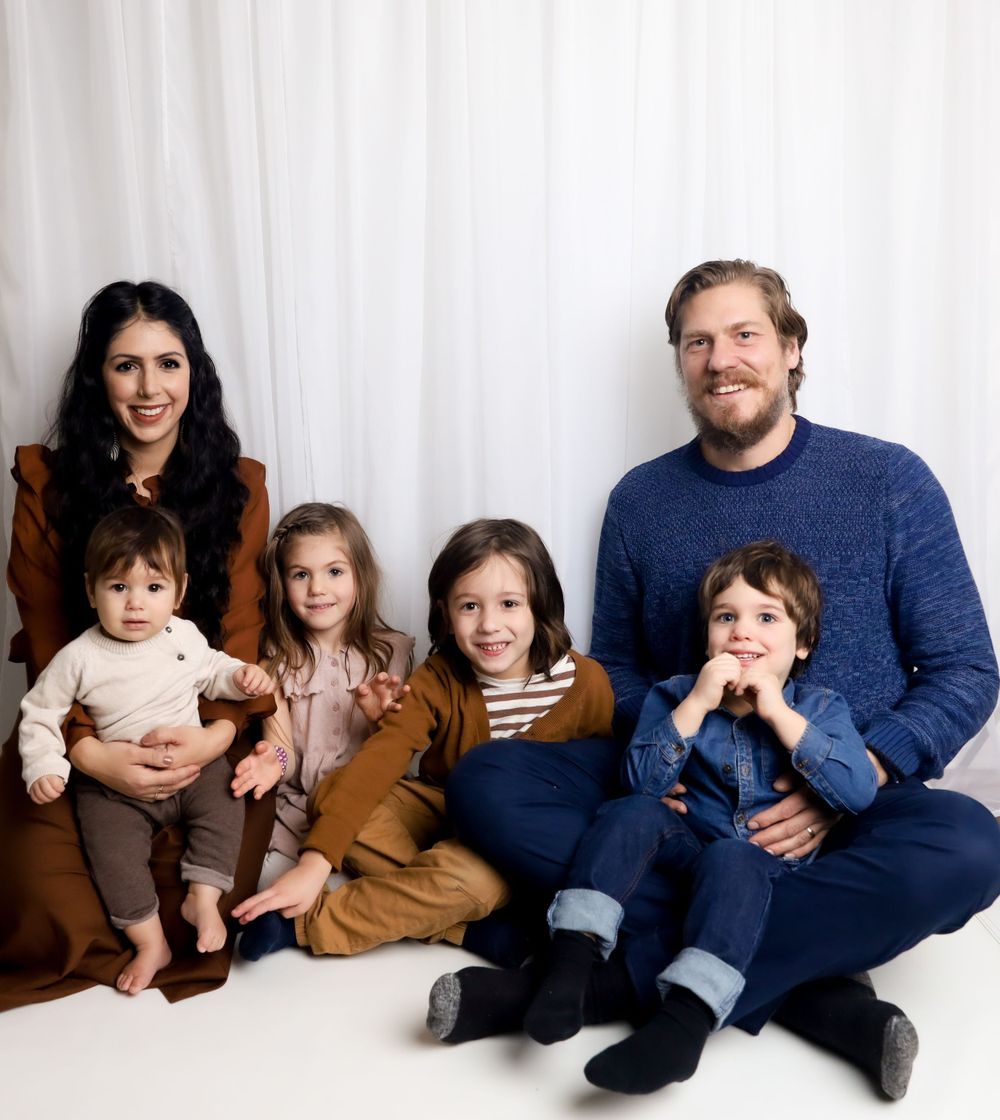 Family portrait featuring four children and parents sitting together against a white backdrop.