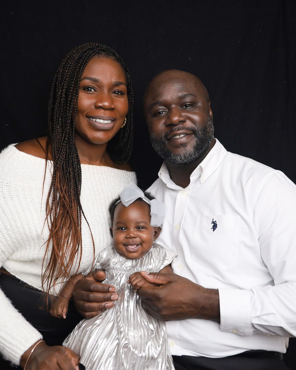 Family portrait against black background wearing coordinated white and cream colored outfits.