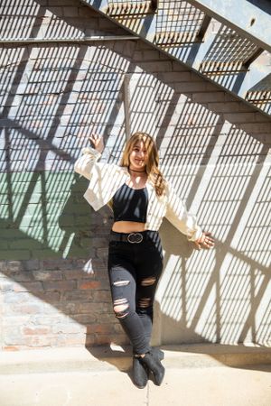 Person in crop top and ripped jeans dancing in sunlit architectural space with dramatic shadows.