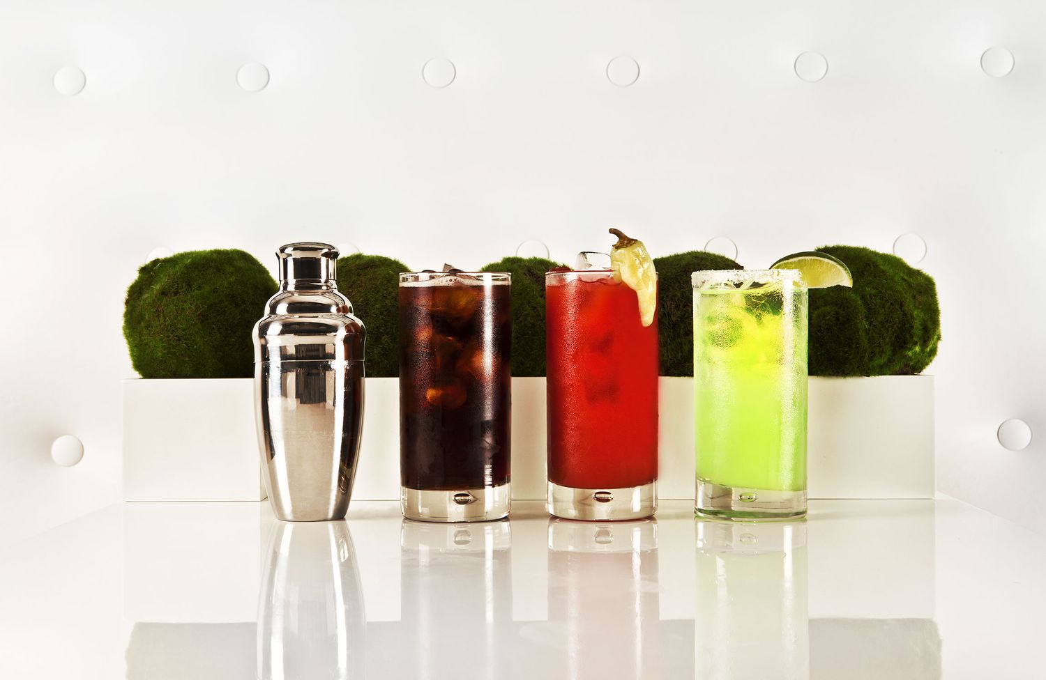 Colorful cocktails and bar tools arranged with limes against white background.