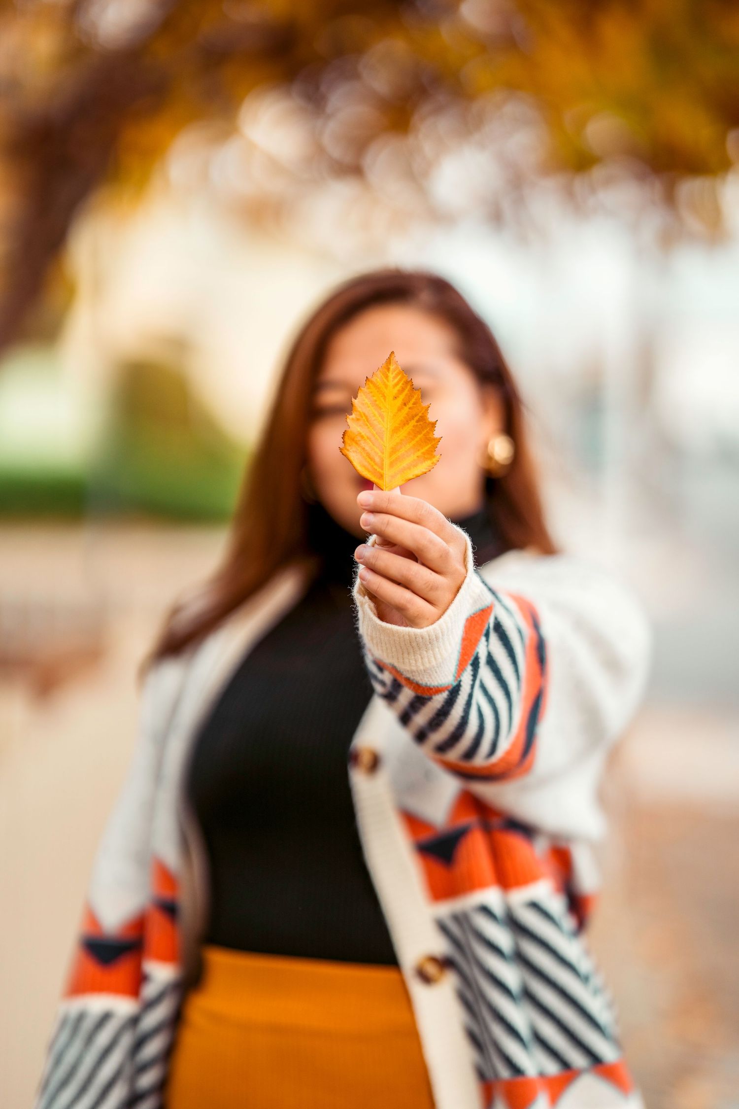 Fashion detail of person holding autumn leaf while wearing geometric pattern sweater and orange skirt.