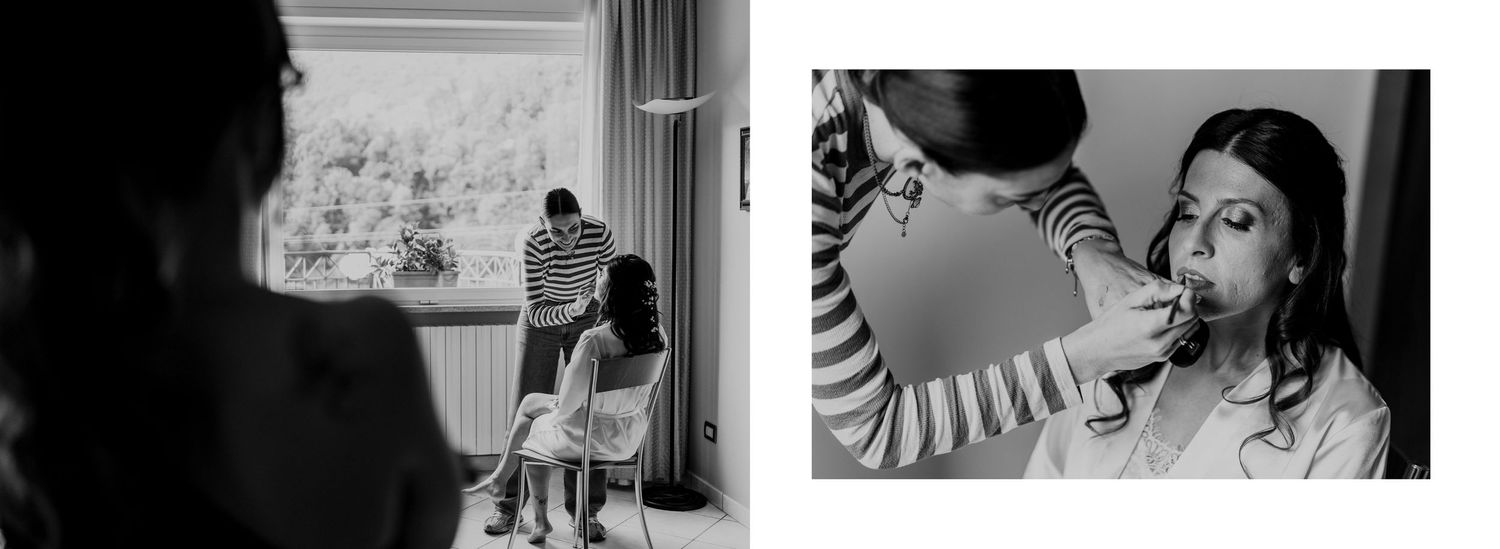 Black and white behind-the-scenes wedding preparation photo of bride getting makeup applied near bright window.