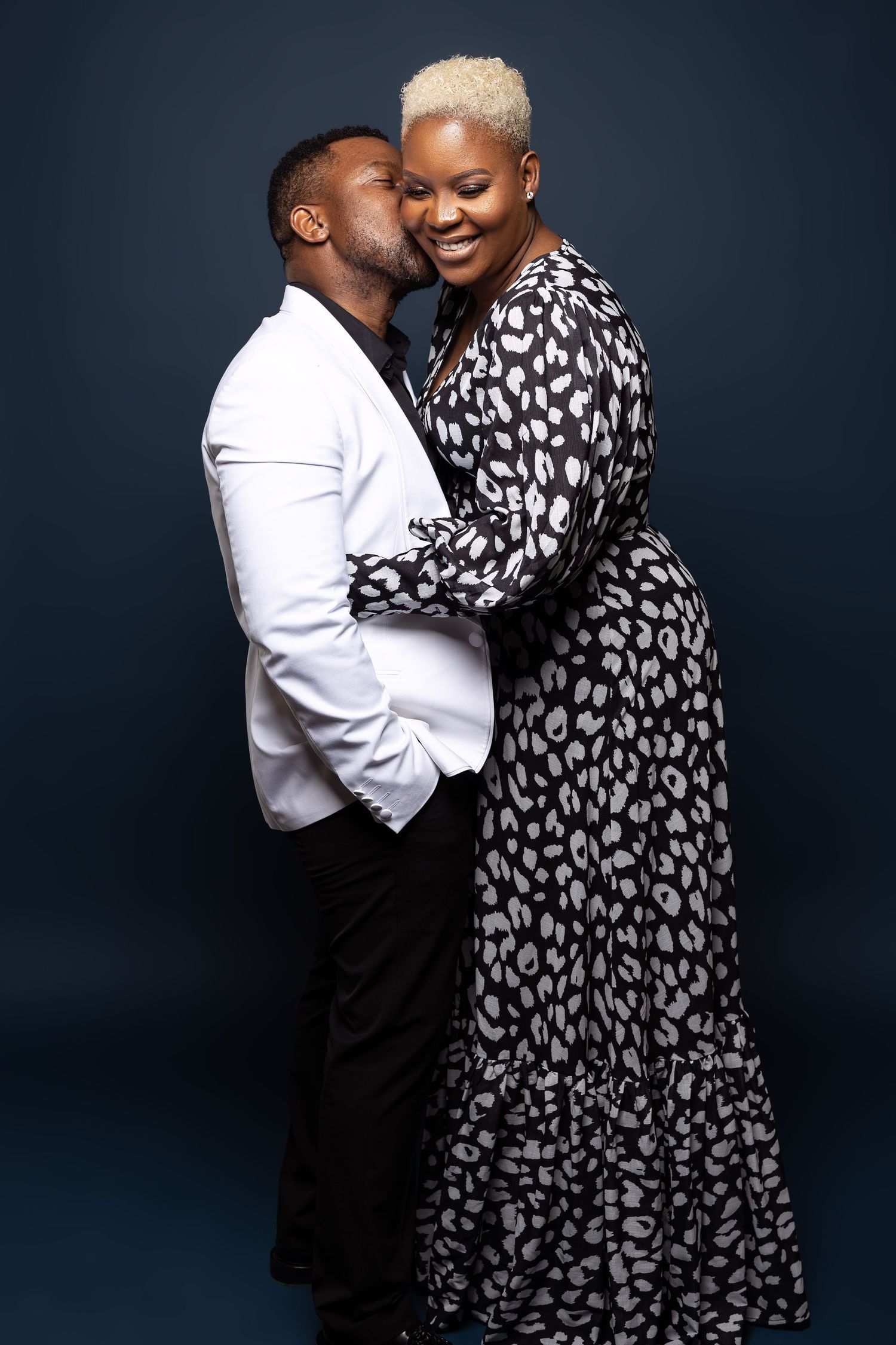 Couple embraces lovingly in contrasting white and patterned outfits during studio photoshoot.