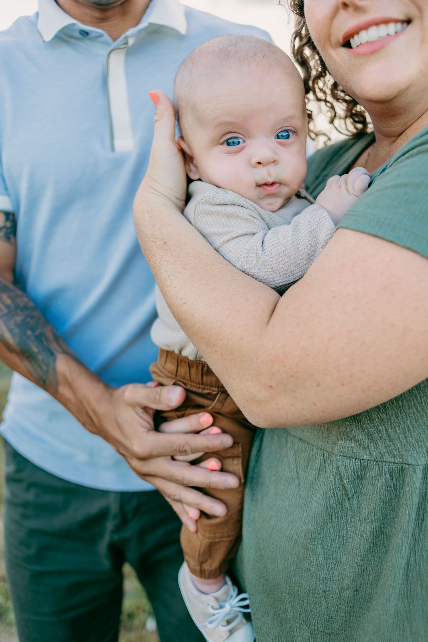 Close-up of young infant being held by parents outdoors during family photoshoot.