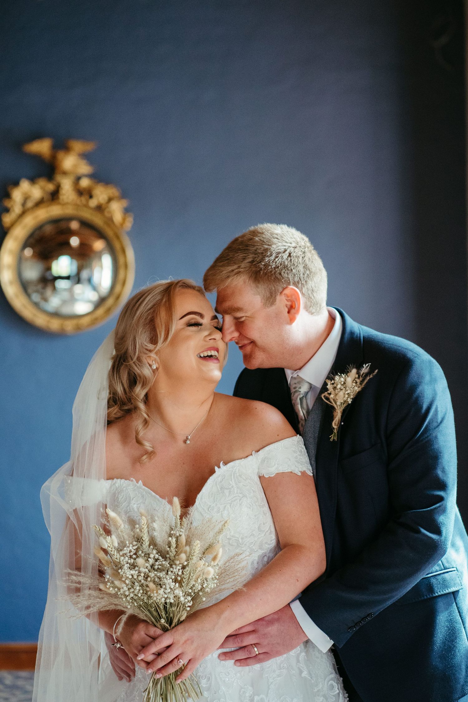 Intimate wedding portrait against dark blue wall with ornate gold mirrors.