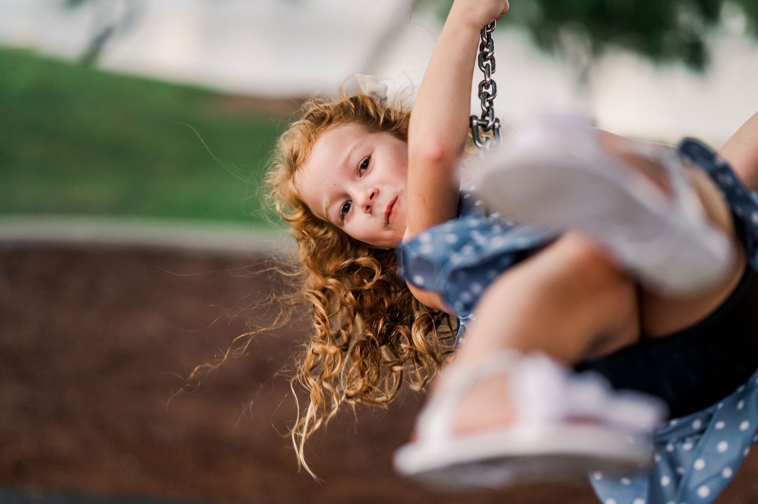 Child with curly hair swinging joyfully at playground in sunlight.