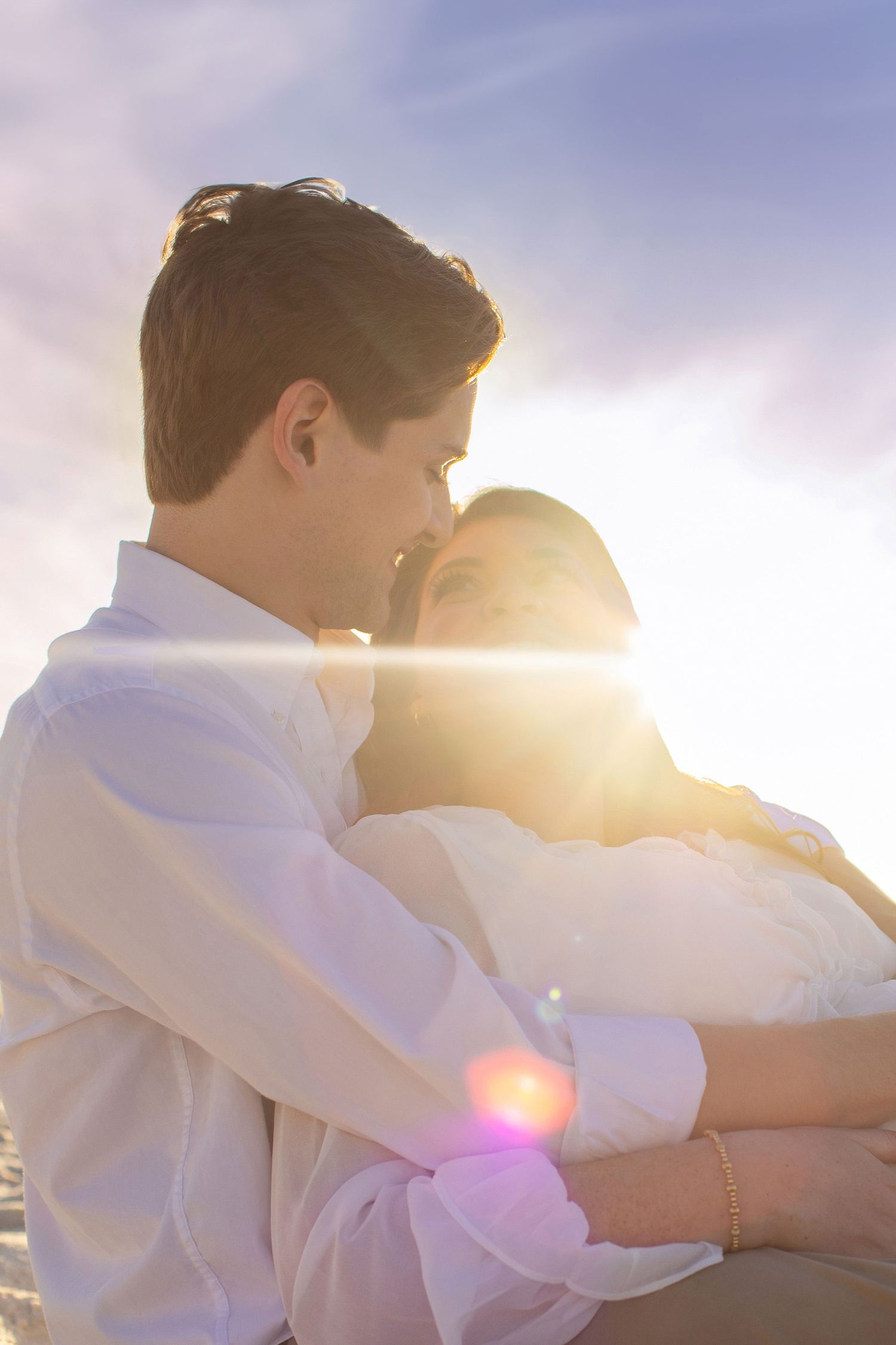 Romantic couple embracing in white clothing during golden hour sunset at the beach.