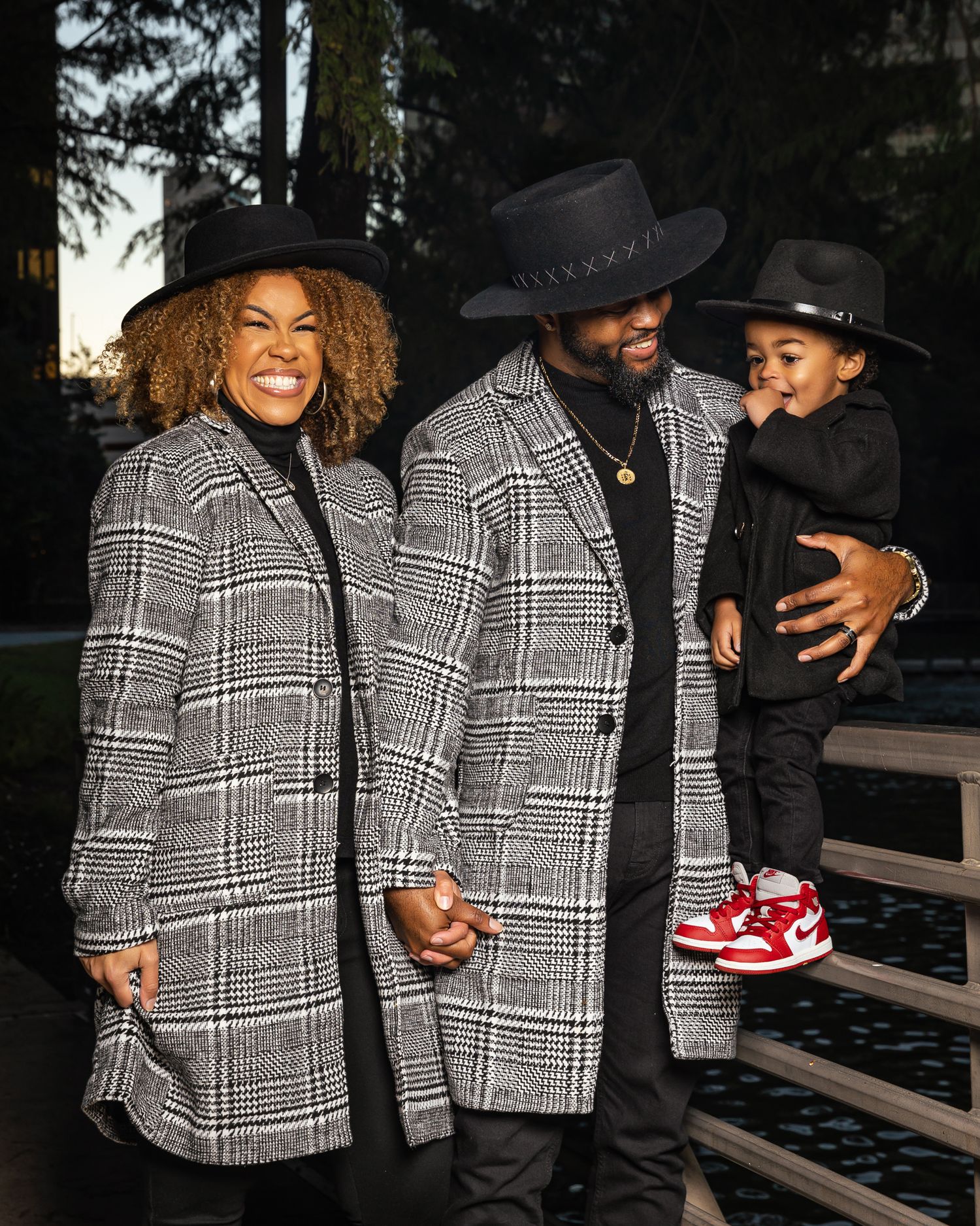 Family in matching plaid coats and black hats pose together outdoors.