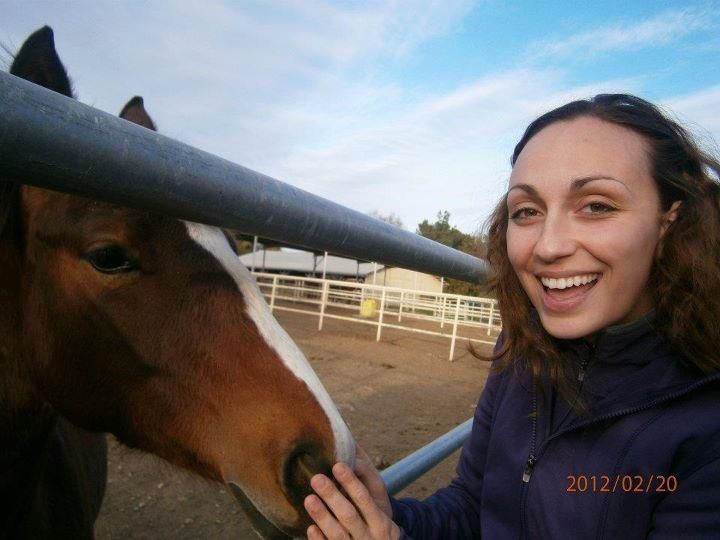 woman smiles at camera while petting horse's nose