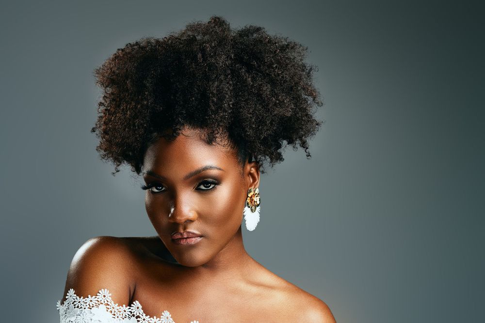 Glamorous beauty portrait featuring natural curly hair and off-shoulder white dress.