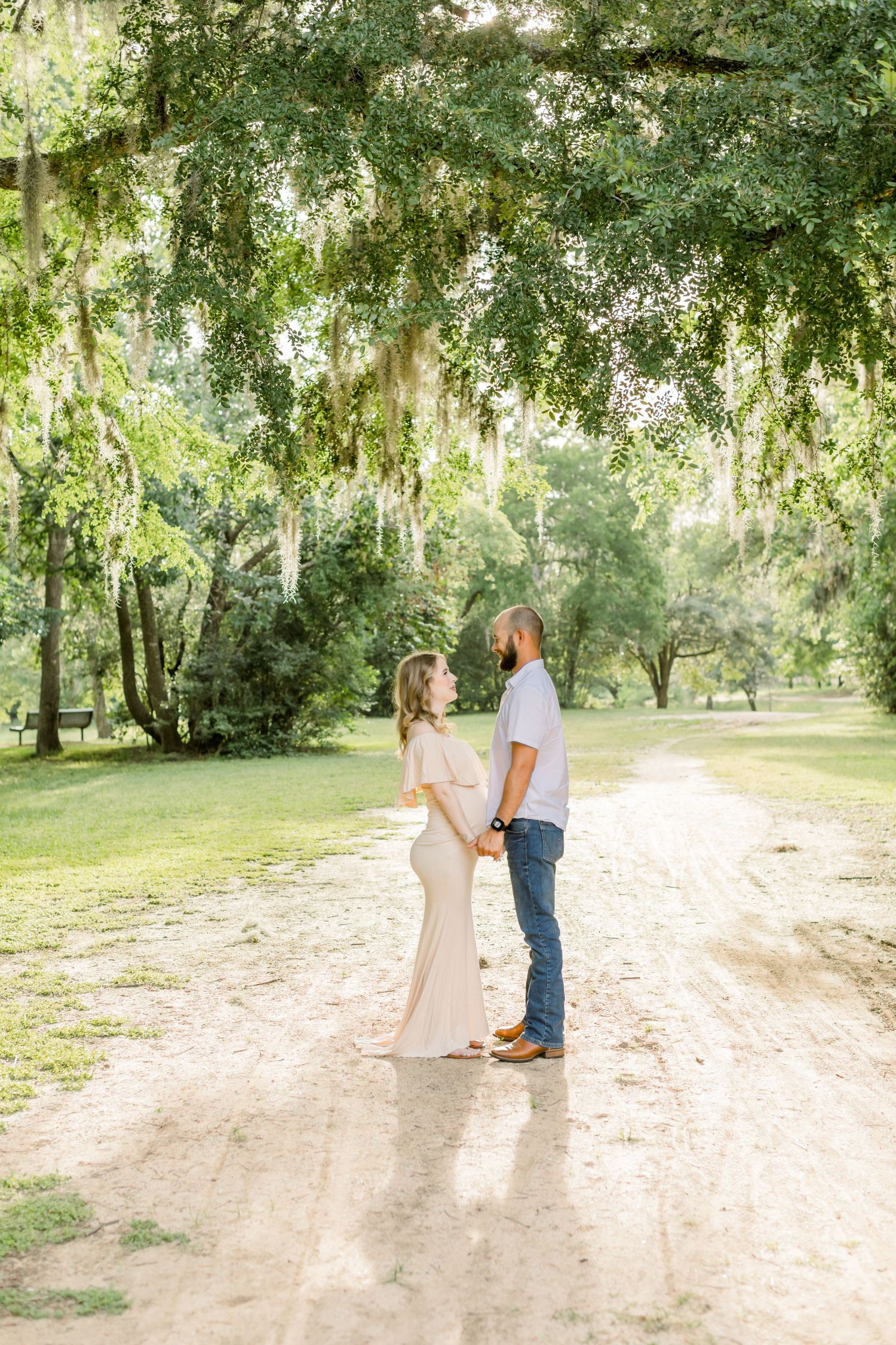 Sunlit maternity portrait beneath overhanging Spanish moss on dirt trail.