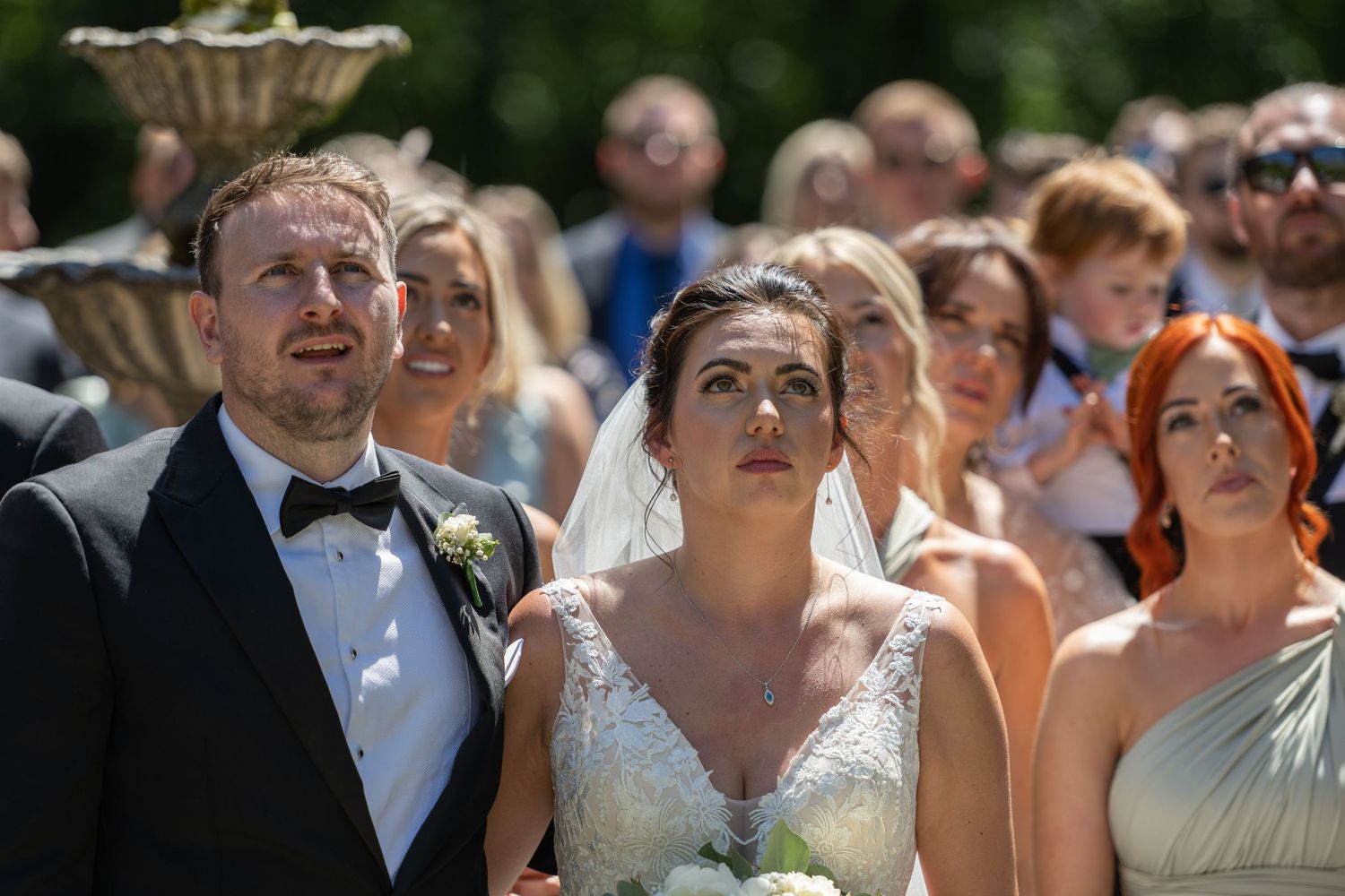 Wedding guests watch with joyful expressions during an outdoor summer ceremony.