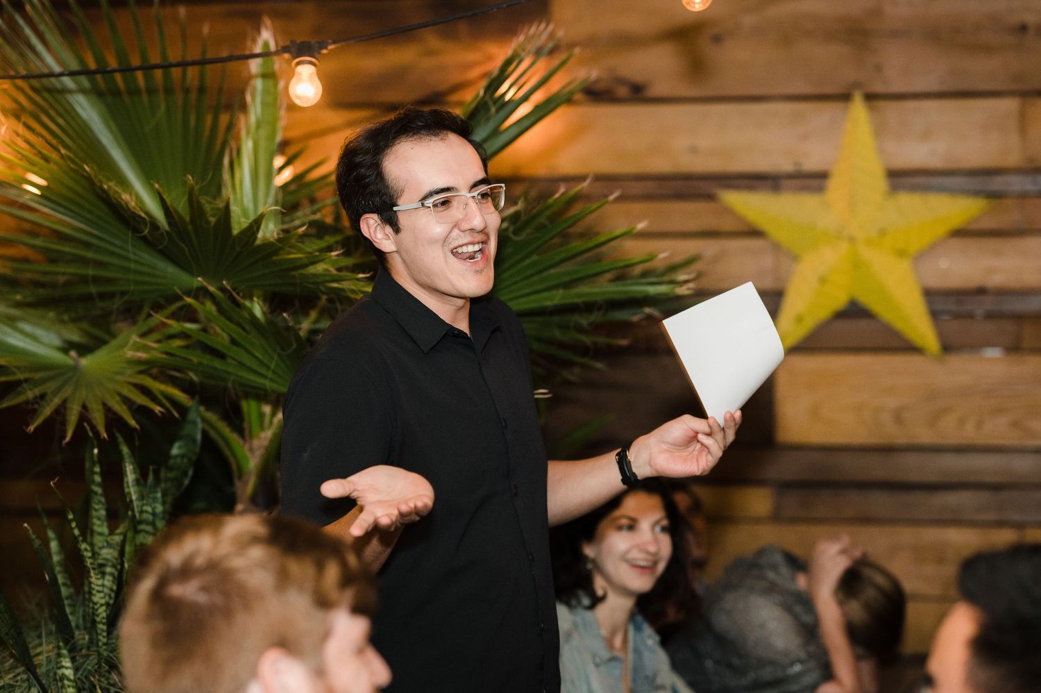 A person gives an animated speech at a reception with decorative stars on wooden walls.