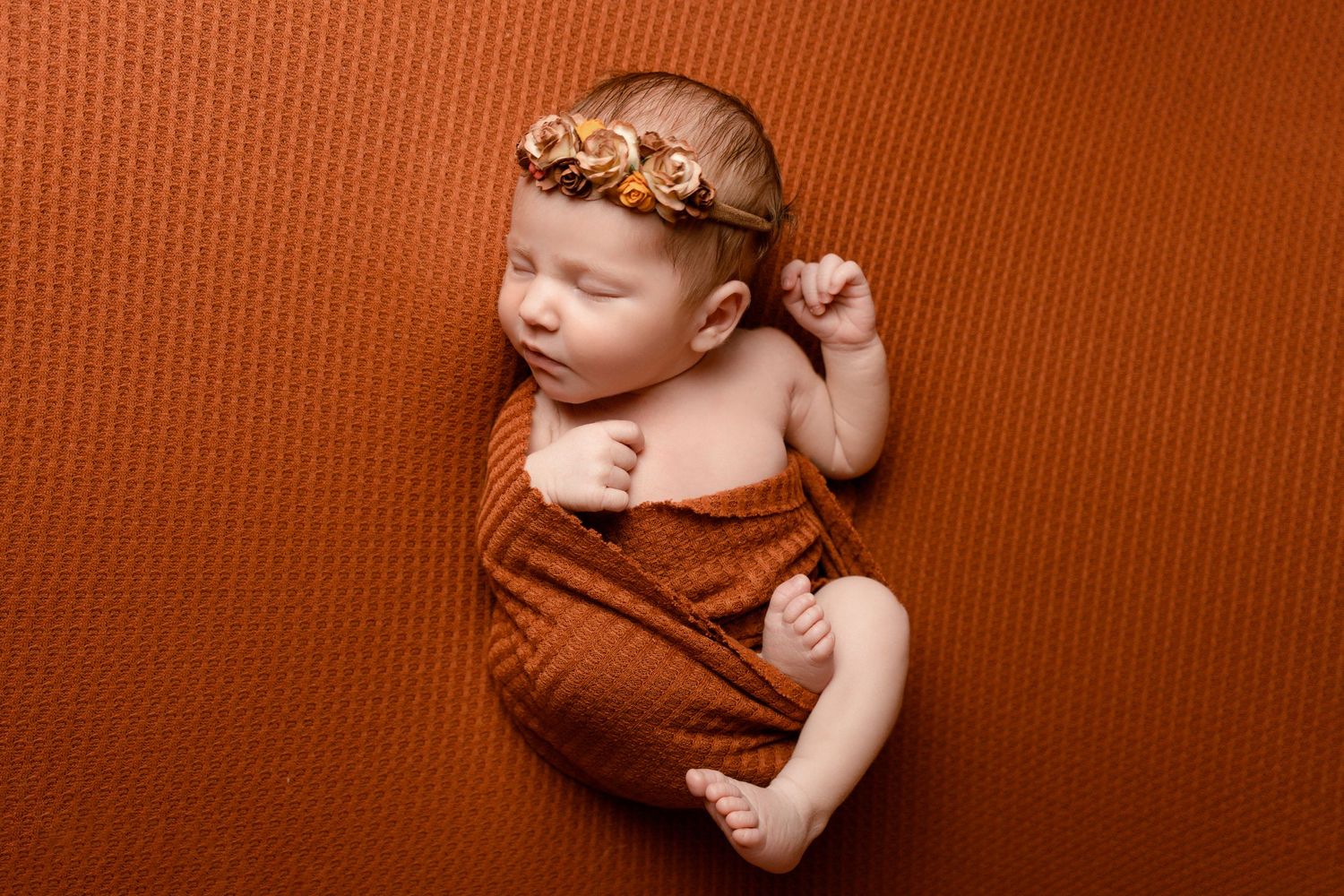 Newborn baby girl wrapped in a copper blanket with autumn floral headband at newborn photoshoot in Doncaster.