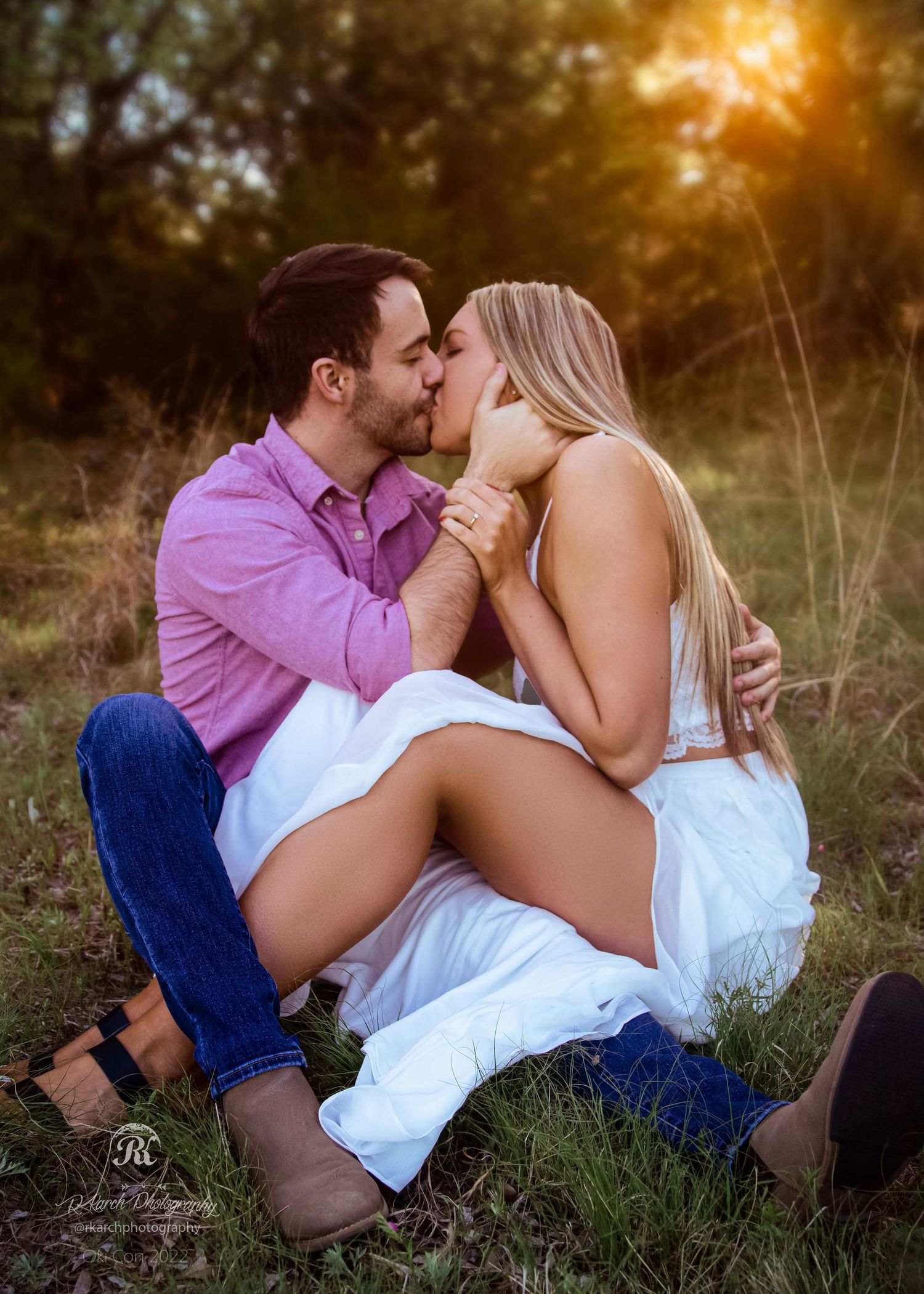 Romantic couple shares an intimate kiss in a sun-drenched field at sunset.