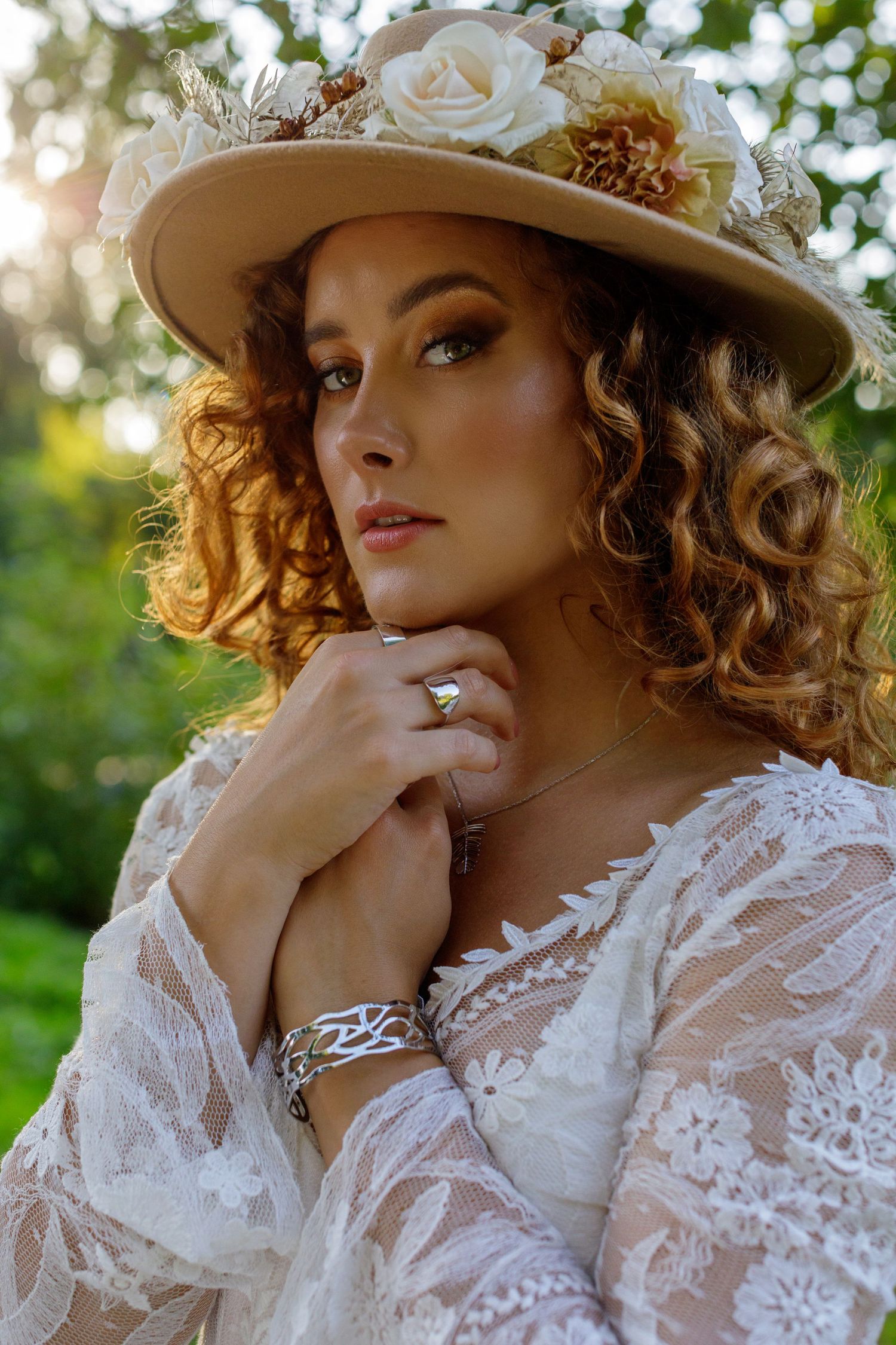 April Pearson posing wearing a boho lace wedding dress and floral hat near a forest clearing in Sussex with sunlight.