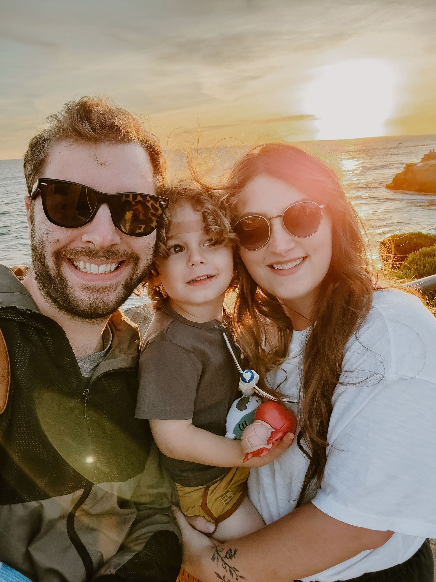 Family taking a sunset selfie together at the beach wearing sunglasses.