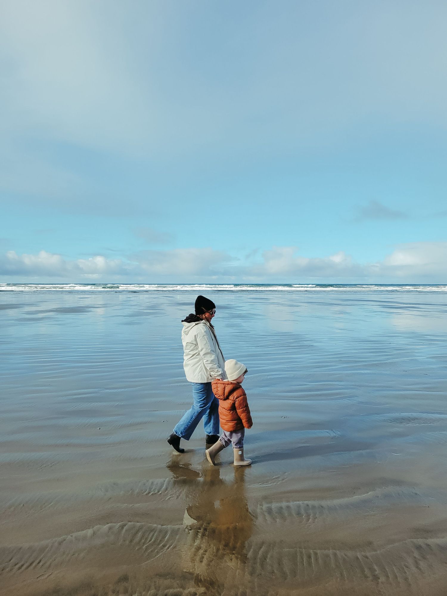 Person in orange jacket exploring and playing on a vast sandy beach during low tide.