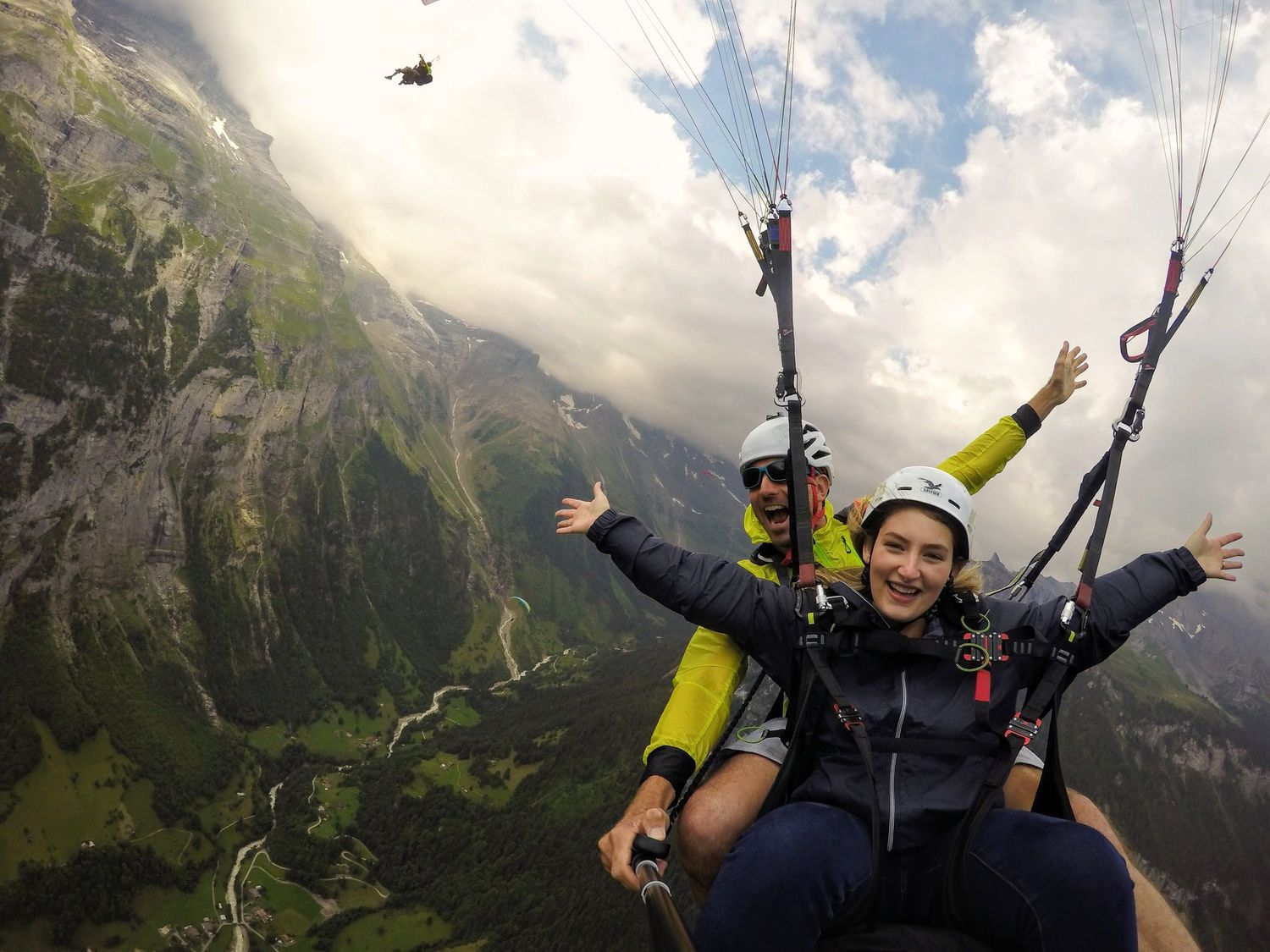 Tandem paragliding adventure over dramatic mountain landscape with cloudy skies.
