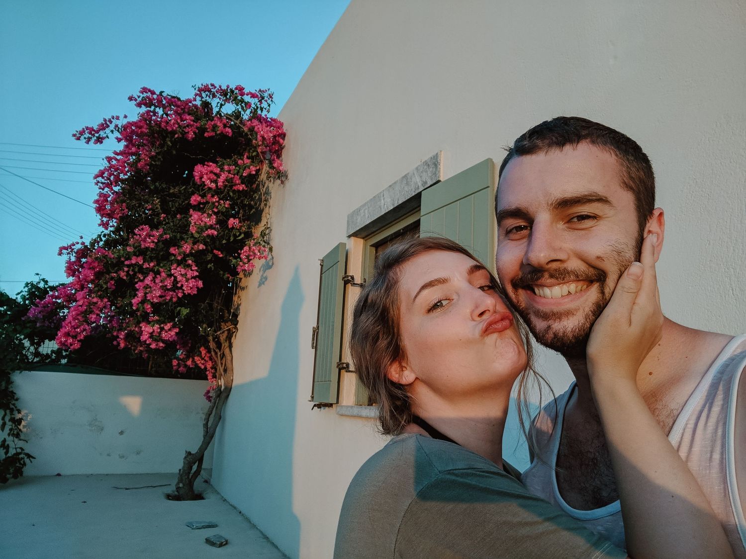 Couple taking selfie in front of white wall with vibrant pink bougainvillea flowers.