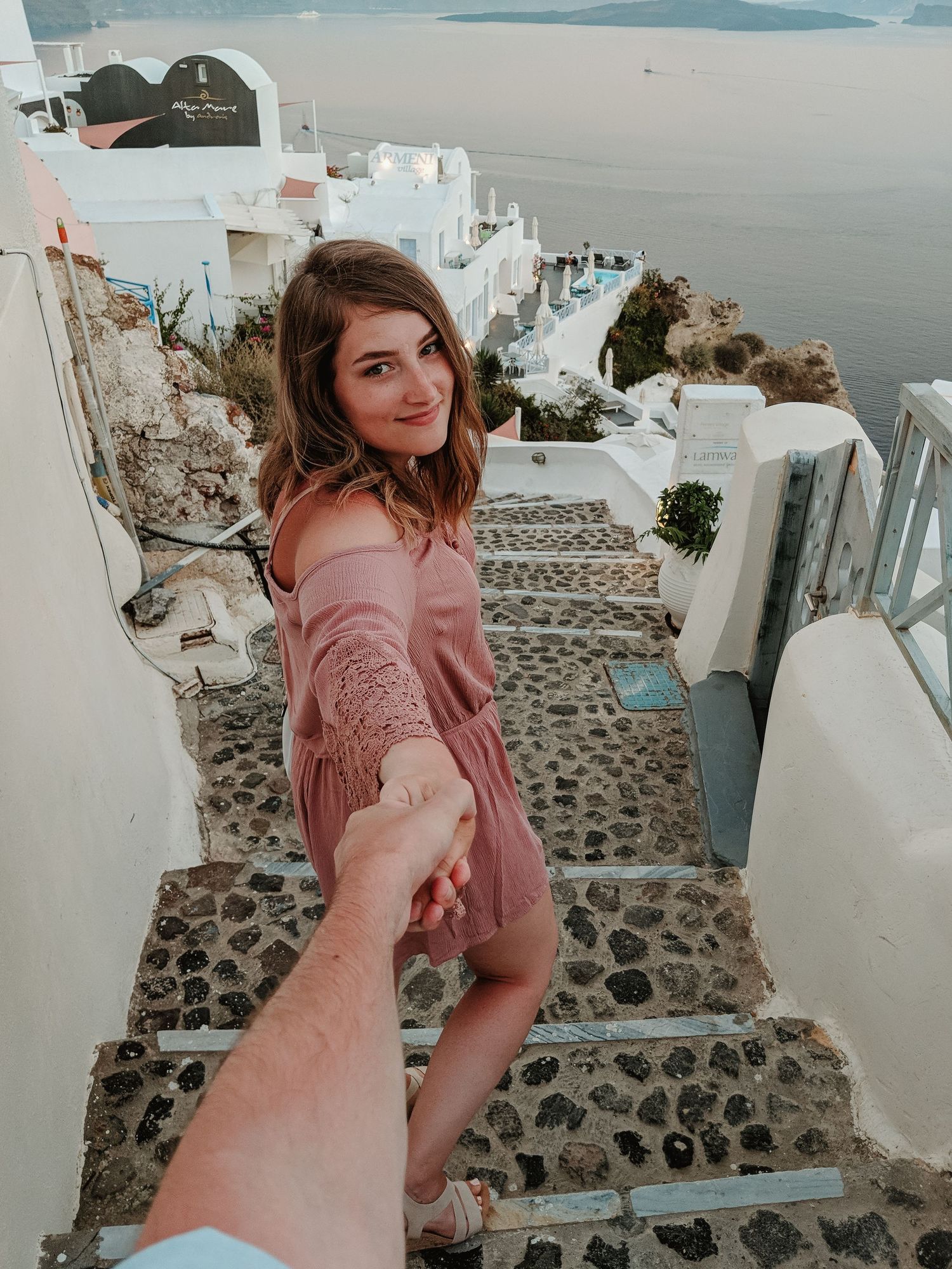 Follow me style photo on white stone steps in Santorini with traditional white buildings and sea views.