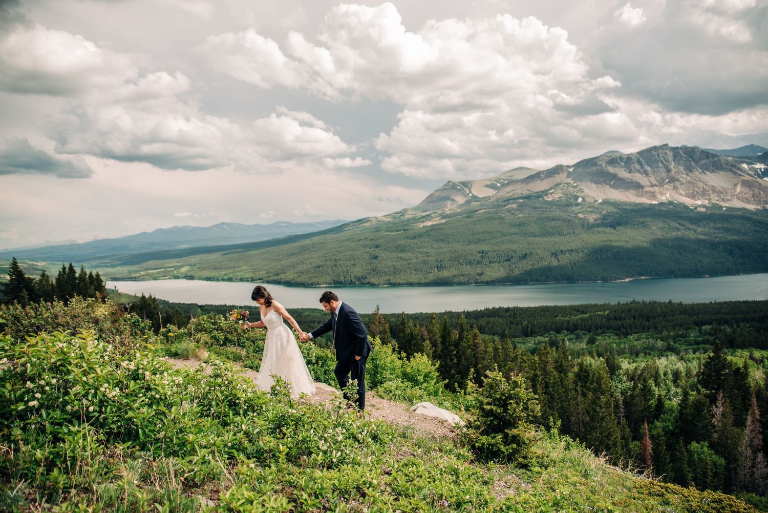 couple in wedding attire holding hands walking up a trail in the two medicine valley of glacier national park
