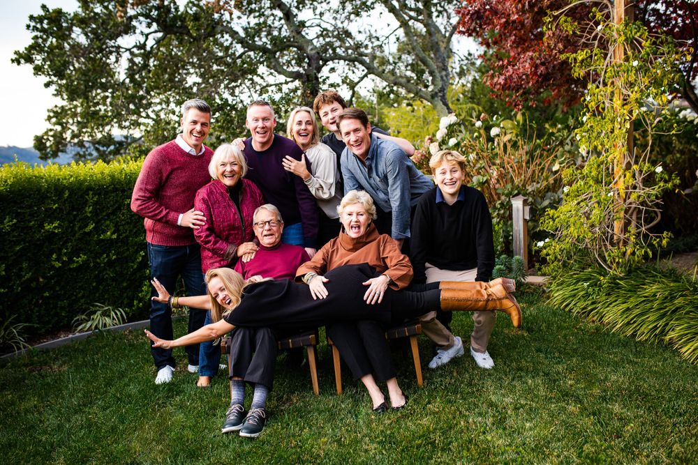 Large multigenerational family smiling together outdoors in a lush garden setting for a group portrait.