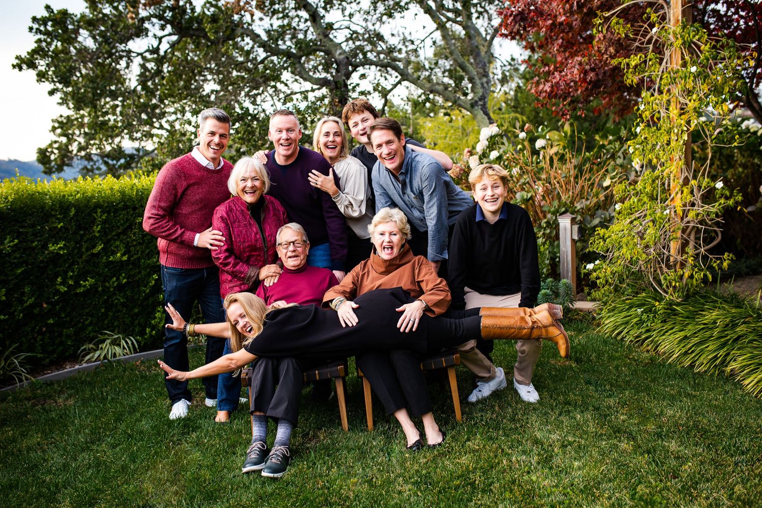 Large multigenerational family smiling together outdoors in a lush garden setting for a group portrait.