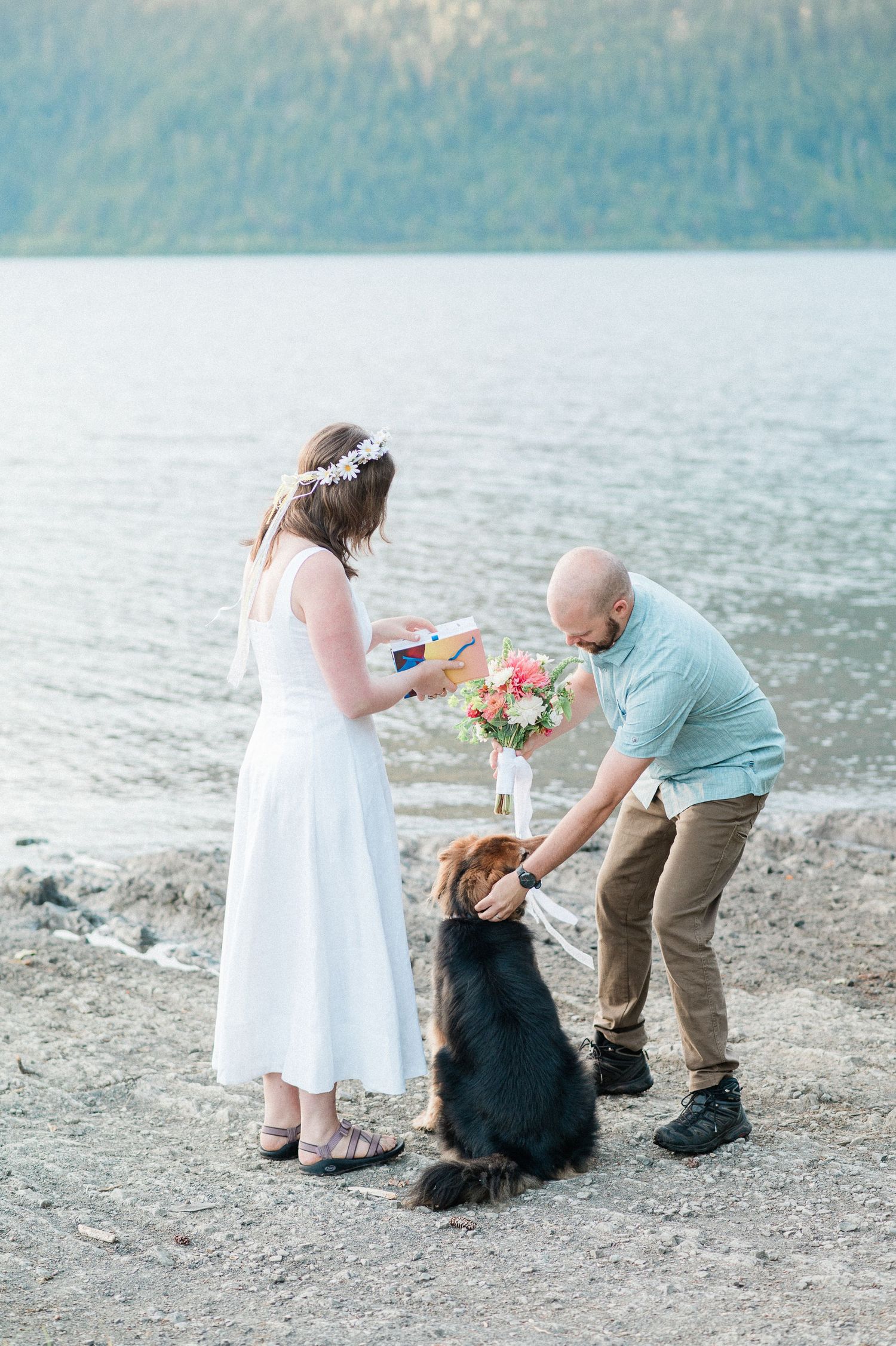 A couple elopes by a lake with their black dog enjoying a peaceful moment together.