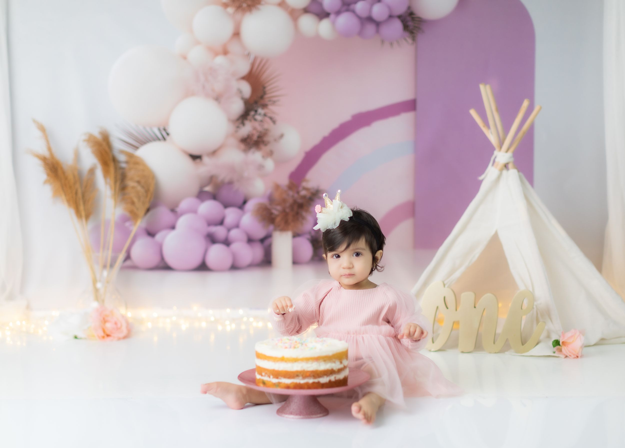 Dreamy first birthday scene with cake and teepee decorations in pink and purple tones.