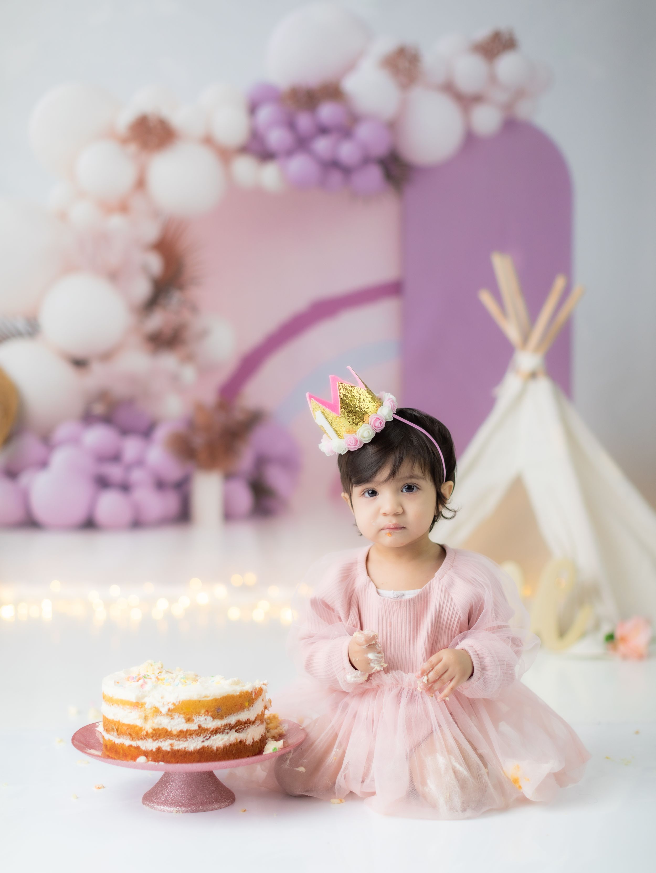 Delicate birthday setup with naked cake and teepee in pink and purple tones.