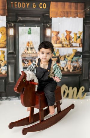 Child playing on wooden rocking horse in front of teddy bear display wall.