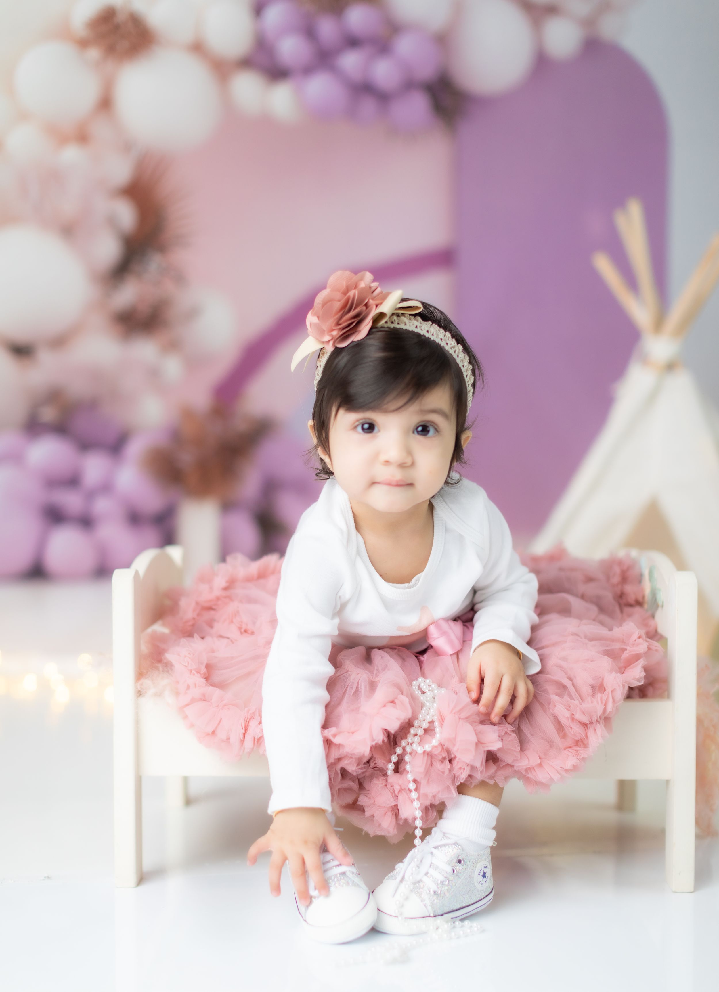 Sweet birthday setup with pink tulle dress and teepee against purple balloon backdrop.