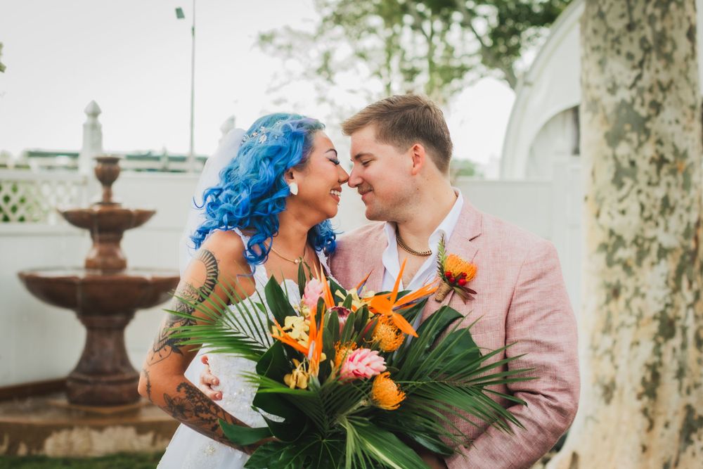 A romantic moment between newlyweds with tropical flowers and a pink suit in an outdoor setting.