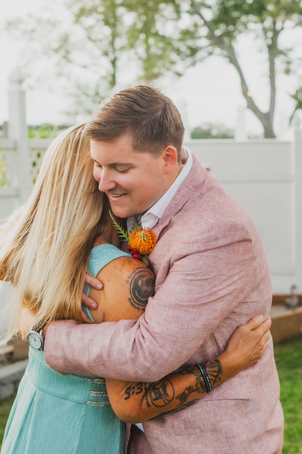 A couple embraces while wearing pink and mint outfits in an outdoor garden setting.