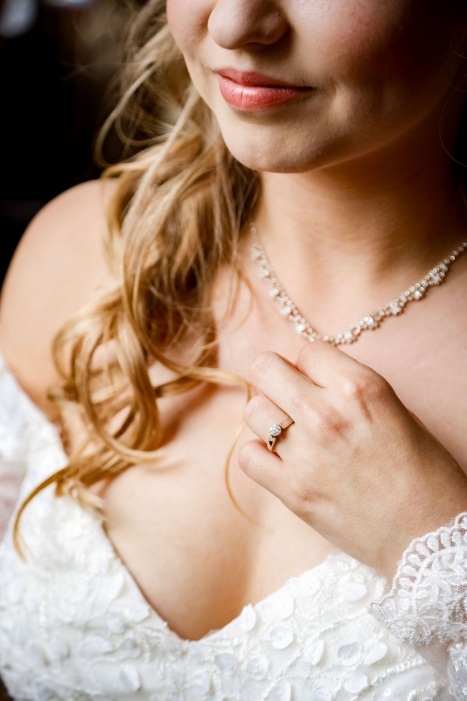 Detail shot of bridal jewelry and lace dress with soft lighting.