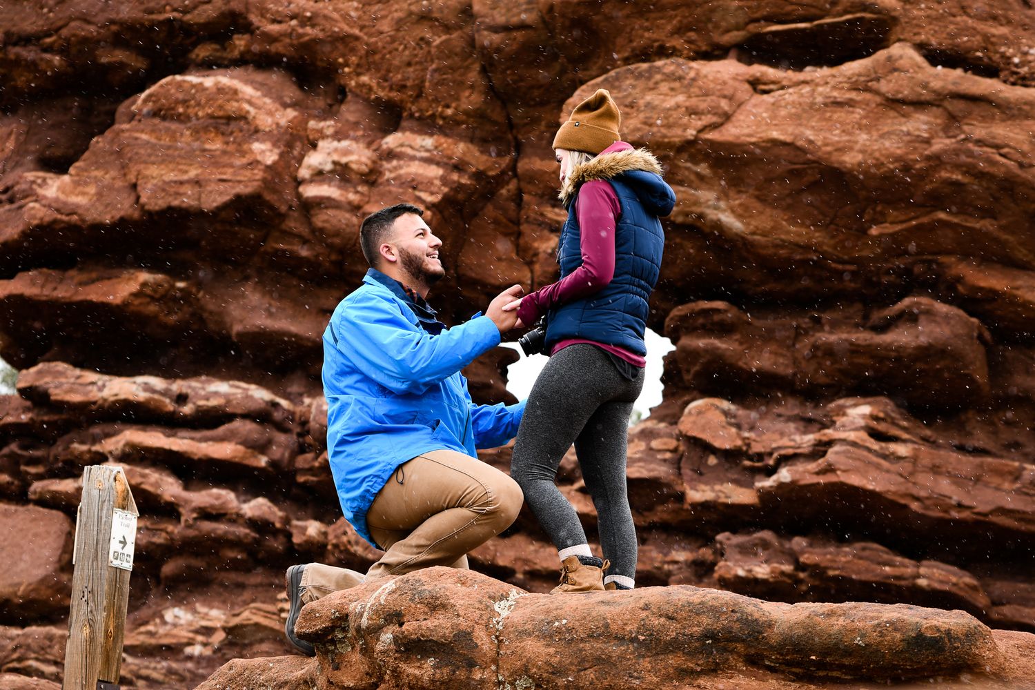 A couple sitting on red rocks and embracing during an outdoor photo session.