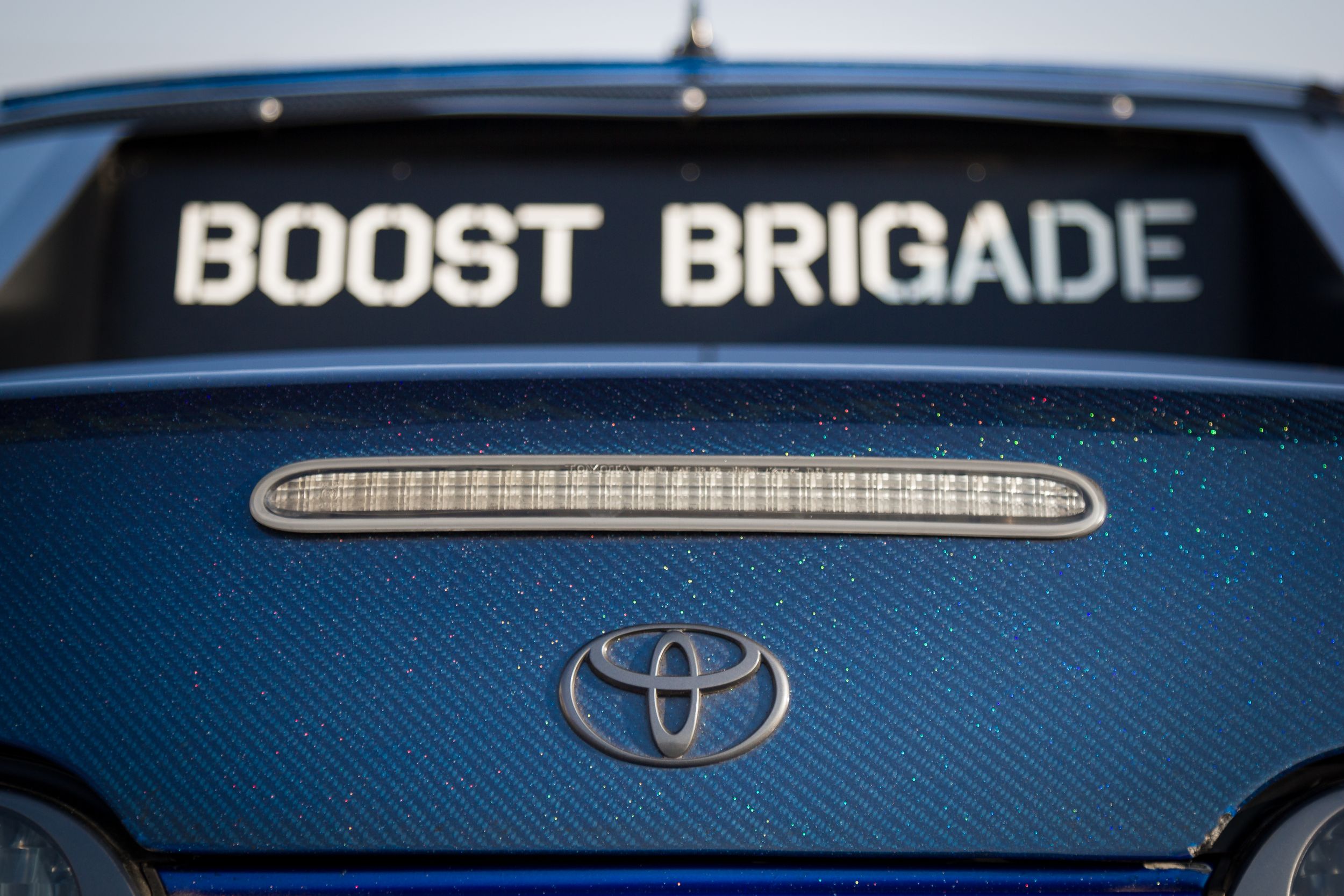 Rear backup lights and Toyota emblem of a Supra with Boost Brigade sticker in the background.