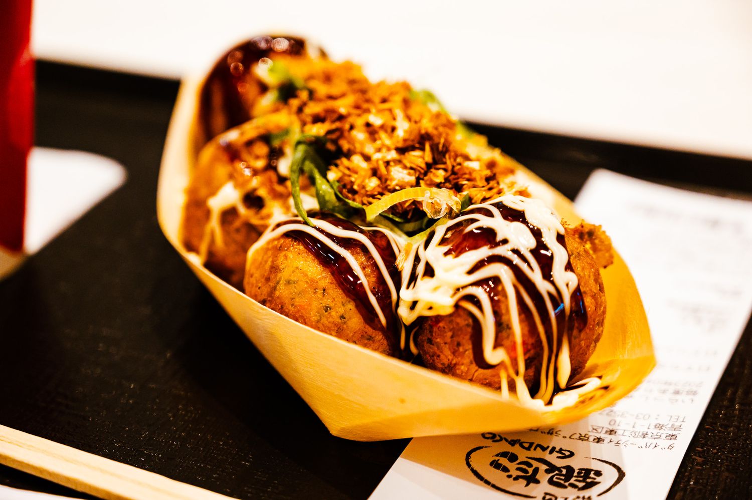 Japanese street food dish with crispy toppings and white sauce served in a wooden boat container.
