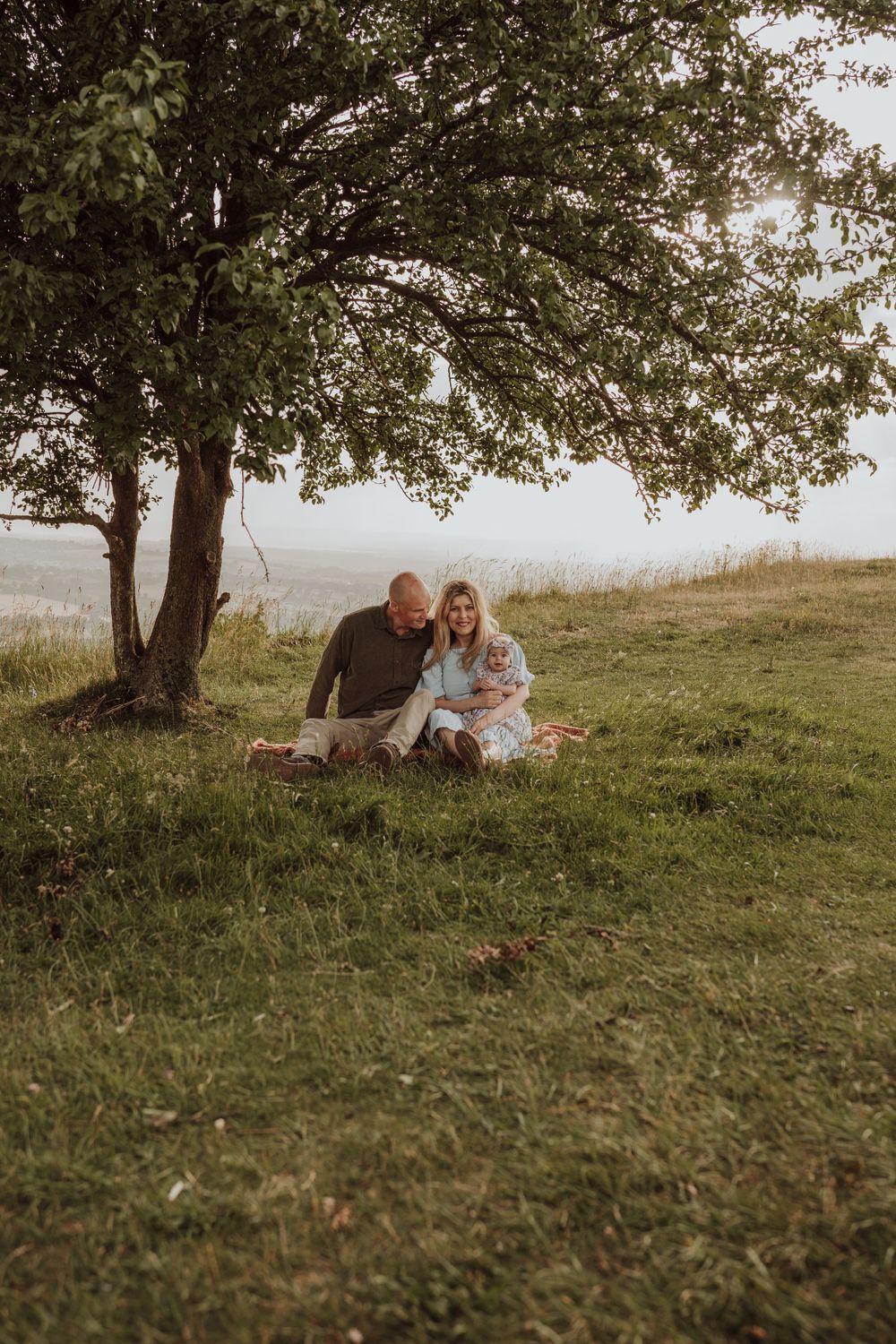 parents cuddle their baby unter tree whilst the sunset in Coaley, Stroud, Gloucestershire