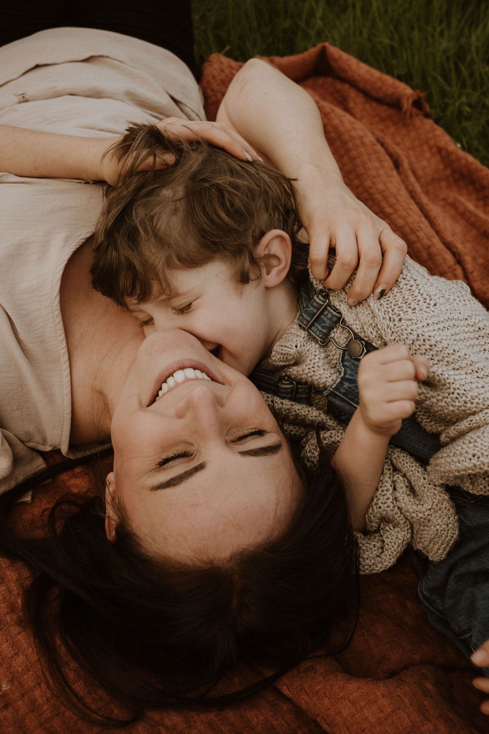 mum and son giggle together whilst laying on a blanket in an open cotswold field
