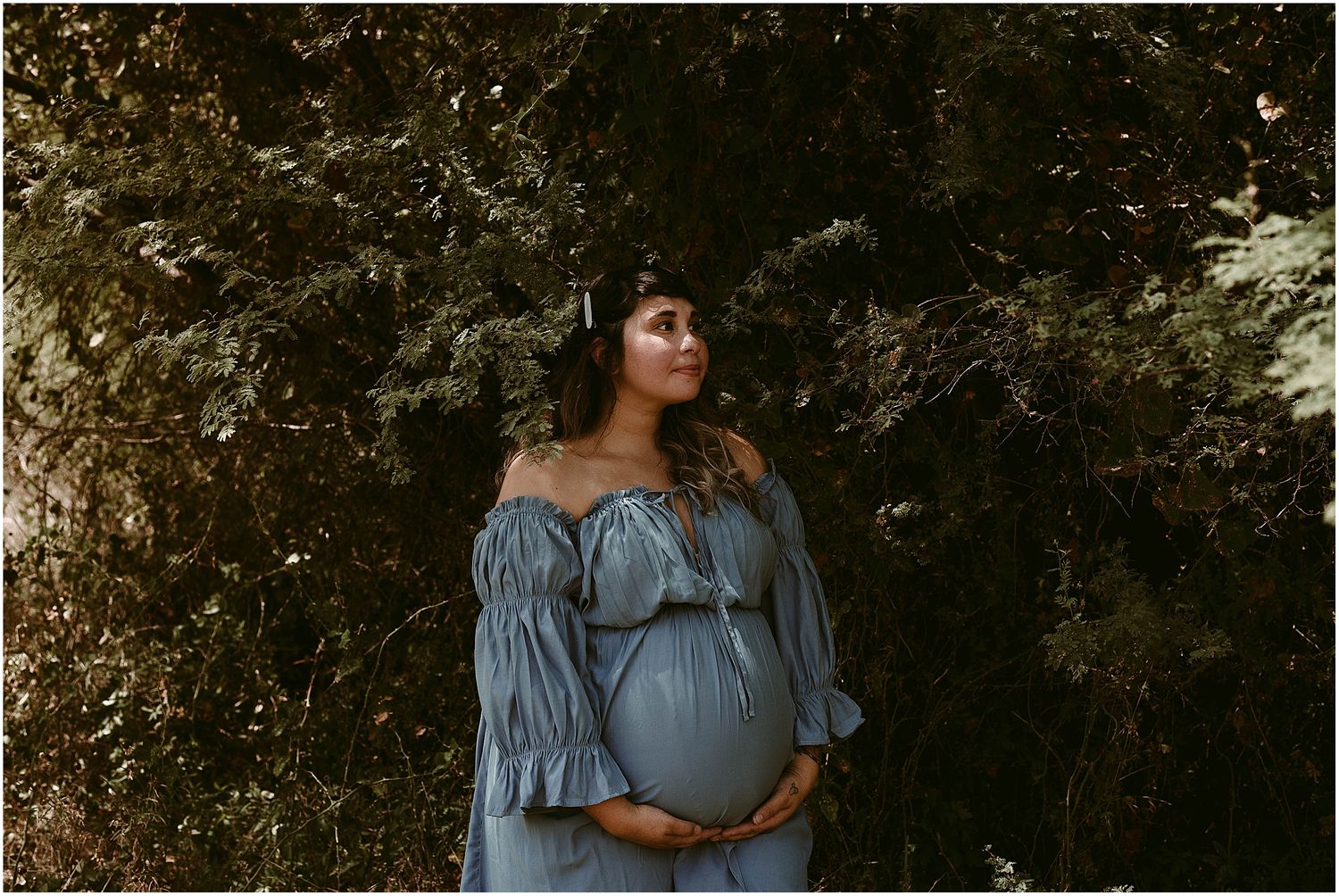 Moody maternity portrait with natural foliage backdrop and blue dress.
