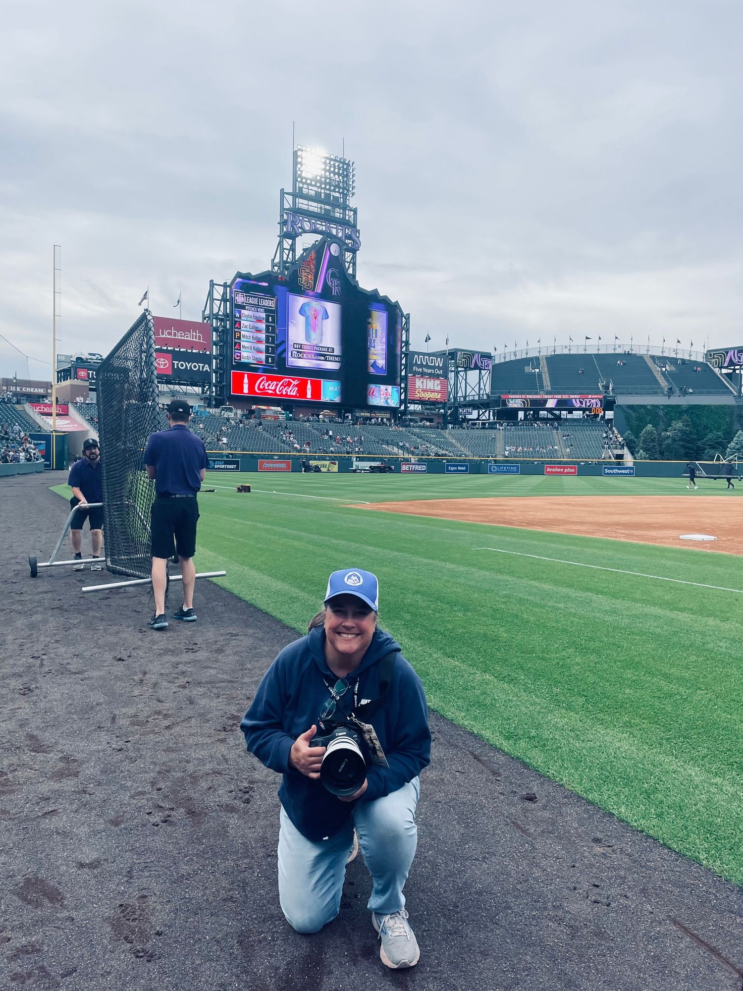 Baseball stadium interior view at Coors Field with photographer on field near warning track on cloudy day.